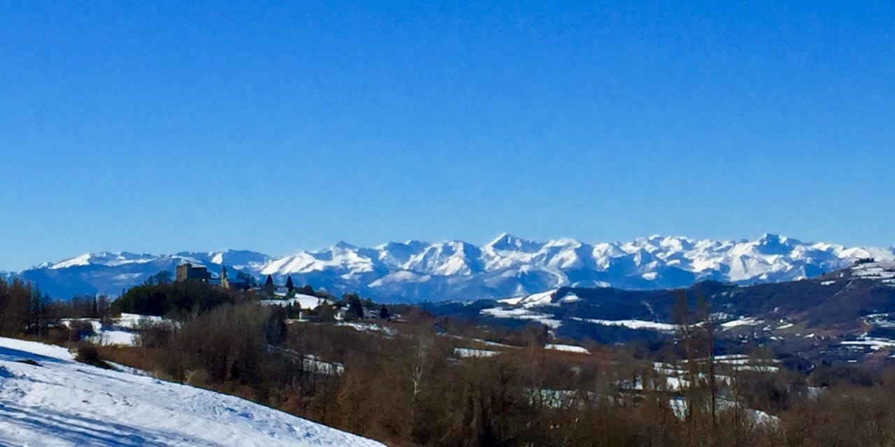 A snowy winter landscape with snow-capped Alps in the background.