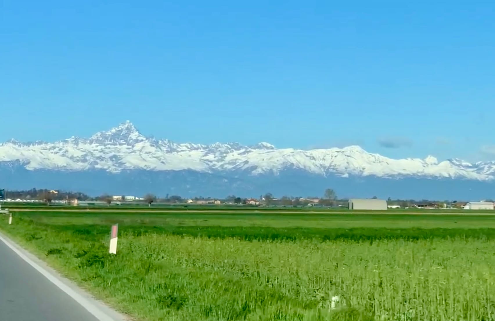 Snow-capped Alps towering over green fields in March.